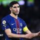 Achraf Hakimi, wearing a blue and red Paris St-Germain shirt, holds out his arms