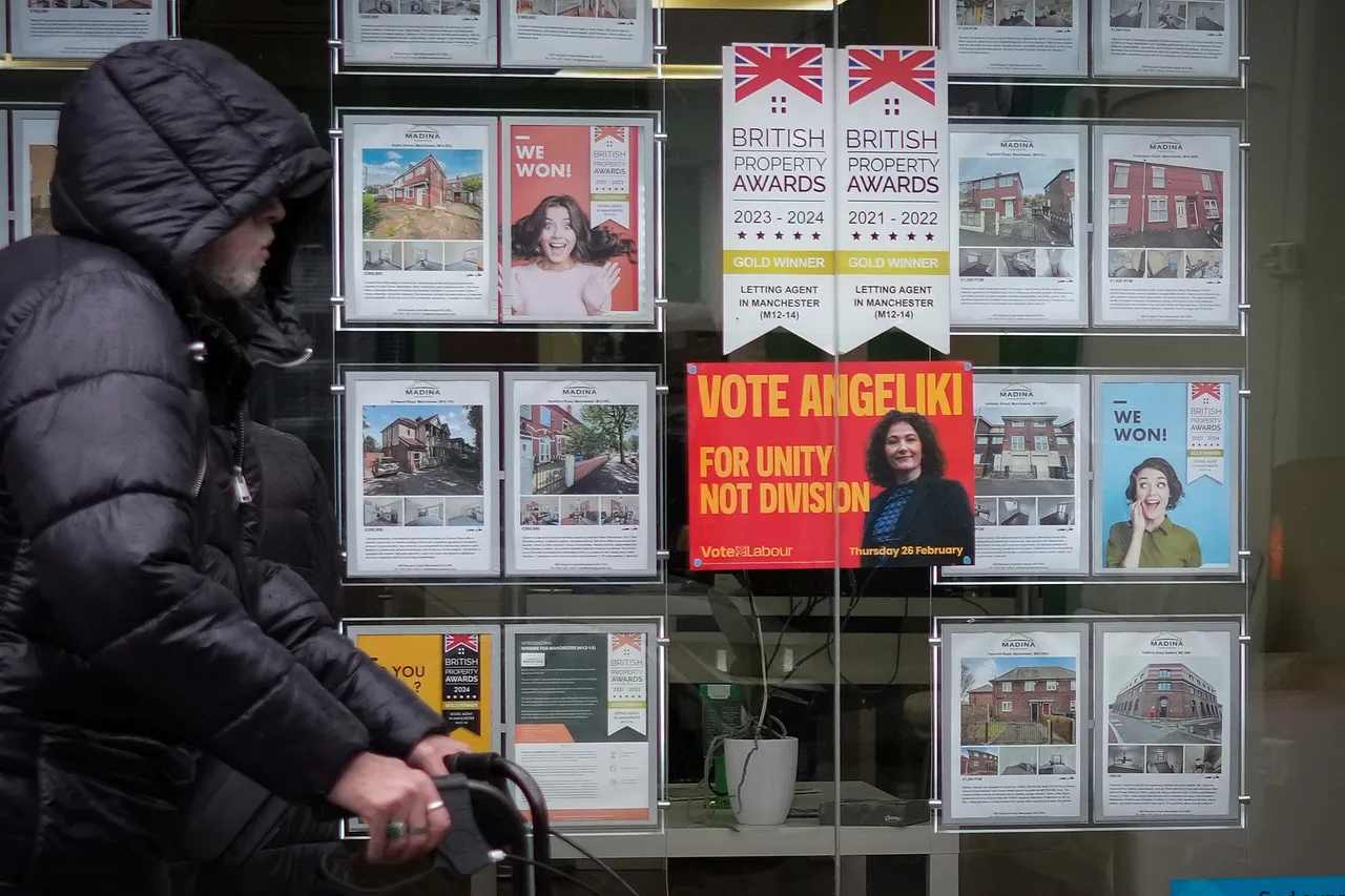 A man walks past a campaign poster for labour candidate Angeliki Stogia in an estate agents window in Longsight on February 11, 2026 in Manchester, United Kingdom.