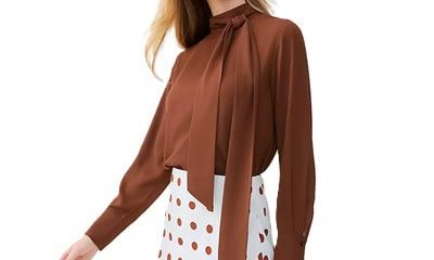 A woman wearing a brown bow-neck blouse with white-and-brown polka dot skirt