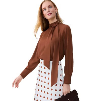 A woman wearing a brown bow-neck blouse with white-and-brown polka dot skirt