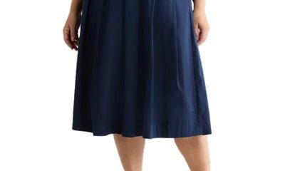 A woman (lower body shown) wearing a dark blue midi skirt, striped top, and brown flats