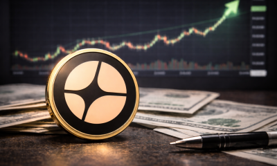 Aster cryptocurrency token placed on dollar banknotes and a desk with a trading chart rising in the background.