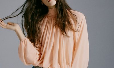 A woman wearing blue jeans, belt, and peach blouse