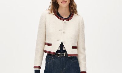 A woman wearing a button-front top with white, red, and black stripes; a lady jacket in cream with red/black trim, a black belt, and dark blue jeans