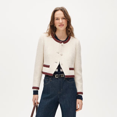 A woman wearing a button-front top with white, red, and black stripes; a lady jacket in cream with red/black trim, a black belt, and dark blue jeans