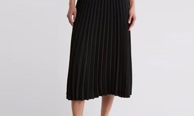 A woman (only the bottom half of her body is shown) wearing a white top, black pleated skirt, and black sandals