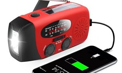 A red hand crank radio / flashlight charging a phone next to it