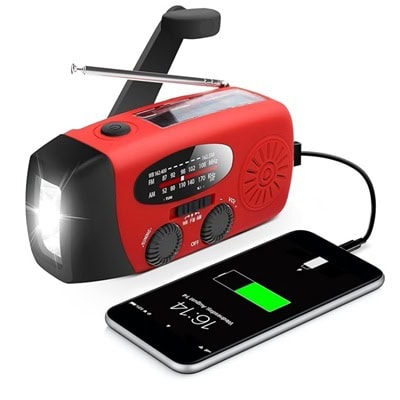 A red hand crank radio / flashlight charging a phone next to it