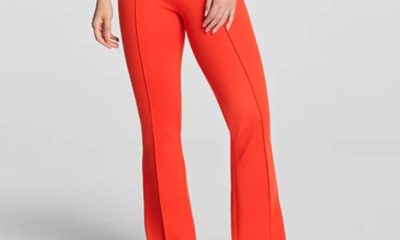 A woman wearing orange pants, black flats, and a white top