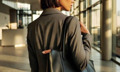 professional stylish Black woman looks out the window; she is wearing a gray suit and has a black leather tote on her shoulder