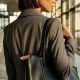 professional stylish Black woman looks out the window; she is wearing a gray suit and has a black leather tote on her shoulder