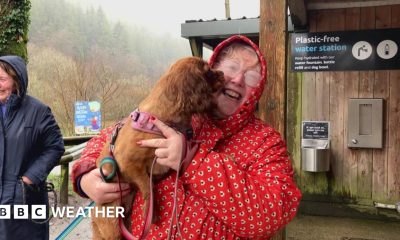 Wet looking woman in red coat holds dog