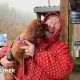 Wet looking woman in red coat holds dog