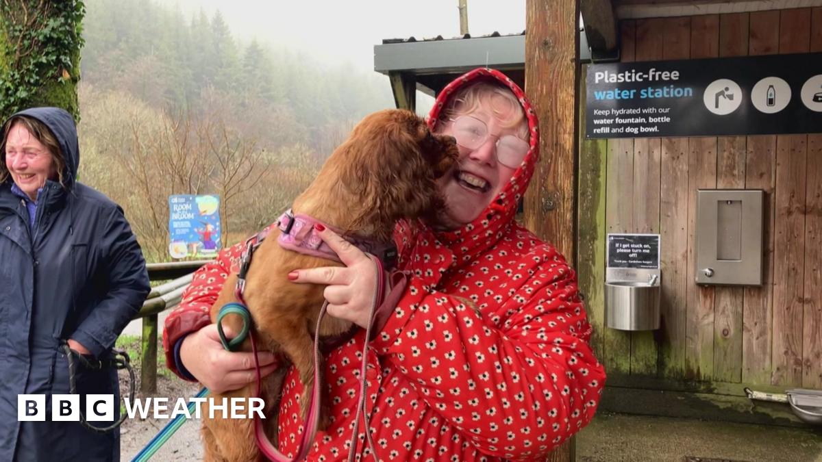Wet looking woman in red coat holds dog