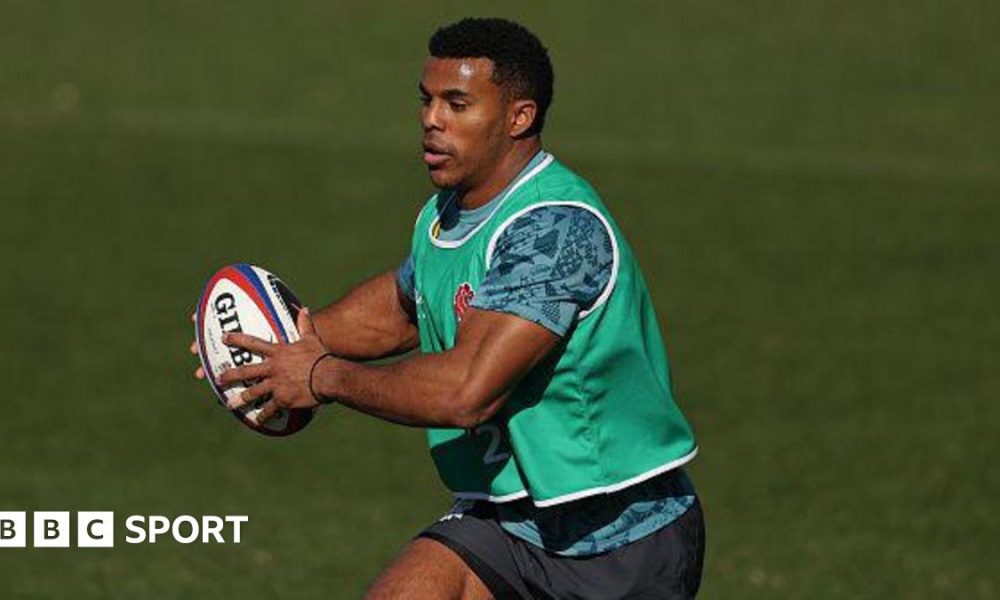 Immanuel Feyi-Waboso running with the ball during an England training camp. He has short black hair and is wearing a green bib with a blue training top and shorts.