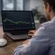 A man looks at a laptop displaying a cryptocurrency price chart, with an Ethereum coin placed on the desk beside him.