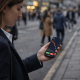 A woman looks at a smartphone showing a sharply declining price chart while standing on a city street.