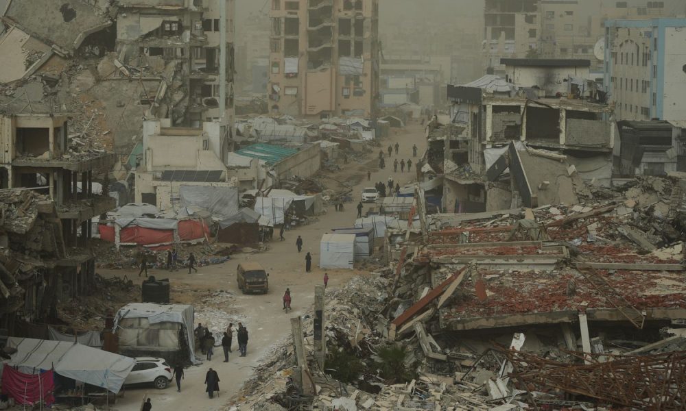 Palestinians walk along a street surrounded by buildings destroyed in recent Israeli air and ground operations. Pic: AP