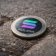 A Solana cryptocurrency coin lies on a rough pavement surface.
