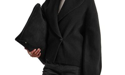 A woman wearing black pants, a white top, black oversized cardigan; she is carrying a black handbag