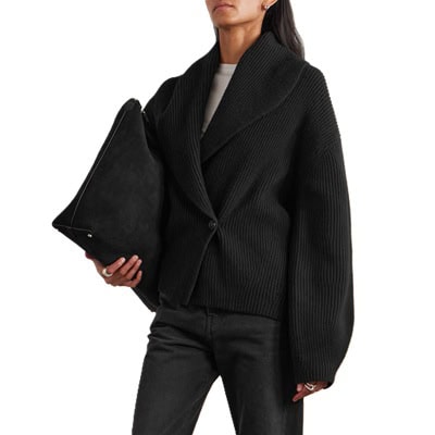 A woman wearing black pants, a white top, black oversized cardigan; she is carrying a black handbag