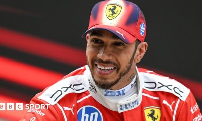 A smiling Lewis Hamilton wearing a Ferrari cap and race overall after he finished third in the Chinese Grand Prix