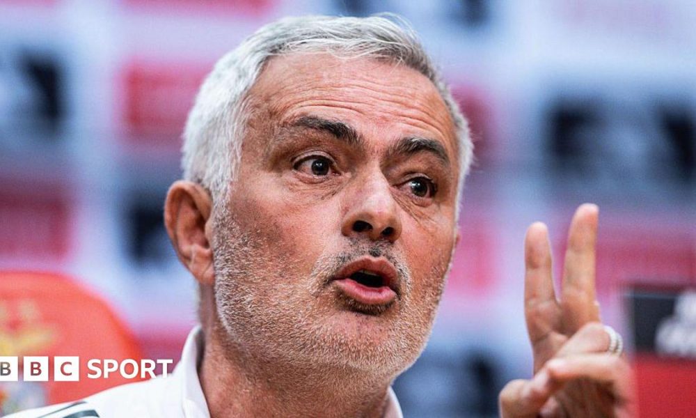 Close-up of Jose Mourinho speaking at a press conference. He has short grey hair, brushed to his right, and stubble. He is gesturing with his left hand.