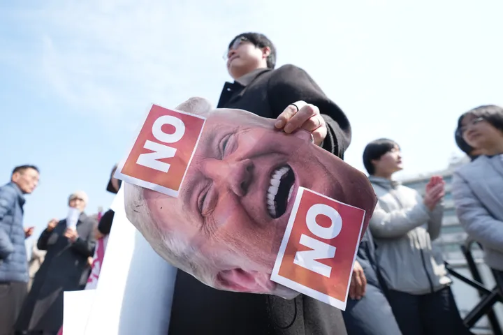 A man holds a picture of U.S. President Donald Trump after a news conference against Trump's demands to multiple countries to send warships to keep the Strait of Hormuz open, near the U.S. Embassy in Seoul, South Korea, on March 16.