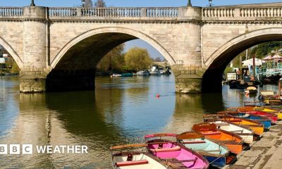 Sunshine reflecting off the water and bridge with a line of colourful row boats lined up on the bank