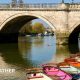 Sunshine reflecting off the water and bridge with a line of colourful row boats lined up on the bank