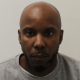 Mug shot of Duane Owusu who has a bald head and beard. He's wearing a crew neck jumper.