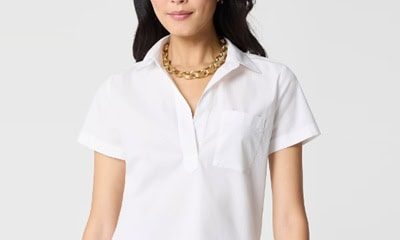 A woman wearing a white short-sleeved top, gold chain necklace, and light blue pants