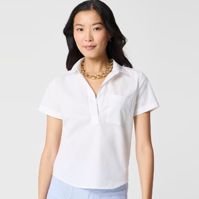 A woman wearing a white short-sleeved top, gold chain necklace, and light blue pants