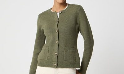 A woman wearing an olive cardigan, ivory pants, and black sunglasses