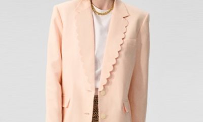 A woman wearing a peach blazer, white top, gold necklace, and brown shorts