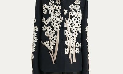 A woman wearing black pants with a black button-front blouse with ivory floral applique