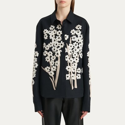 A woman wearing black pants with a black button-front blouse with ivory floral applique