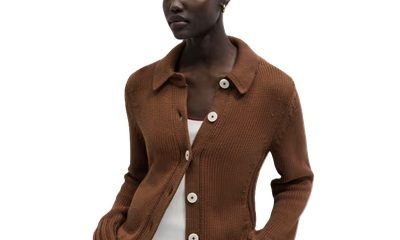 A woman wearing a brown cardigan, white top , and blue jeans