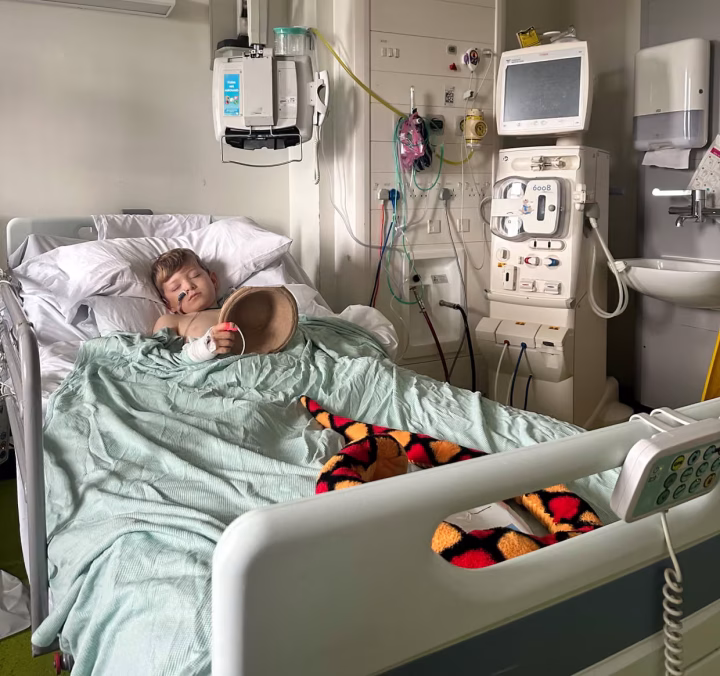 Rex Early rests in a hospital bed, holding a cardboard sick bucket. There's a soft toy snake at the end of his bed.