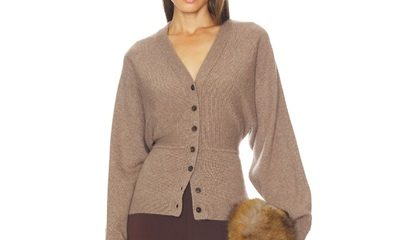 A woman wearing a light brown cardigan, dark brown pants, and holding a fur clutch