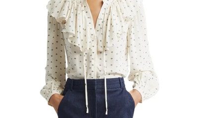 A woman wearing a ruffle-front ivory printed top and tailored denim pants