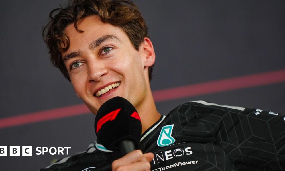 A smiling George Russell speaking into an F1-branded microphone during a news conference at Bahrain testing