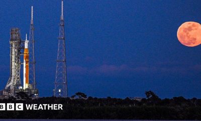 Artemis II rocket on the launch pad in Cape Canaveral with a full, bright and orange Moon rising in the sky next to it
