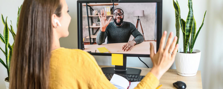 businesswoman waves at a colleague she's meeting with in a Zoom call