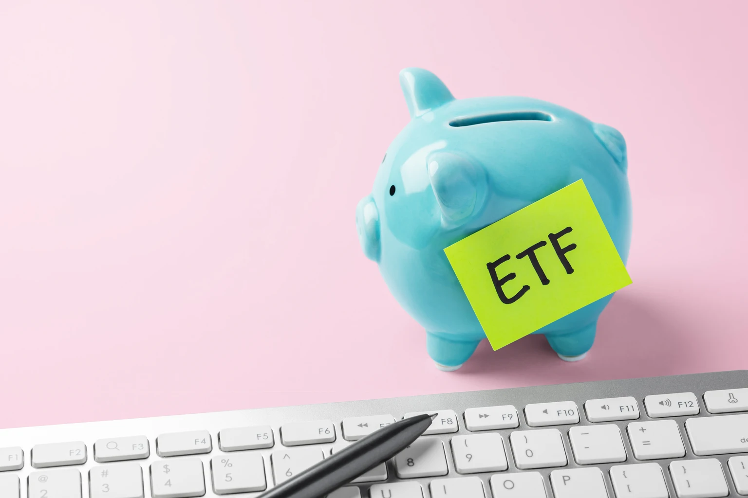 Financial planning and savings for ETF investment. Piggy bank and computer keyboard on pink background