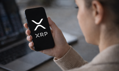 Person holding a smartphone displaying the XRP cryptocurrency logo while checking digital asset markets.