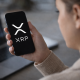 Person holding a smartphone displaying the XRP cryptocurrency logo while checking digital asset markets.