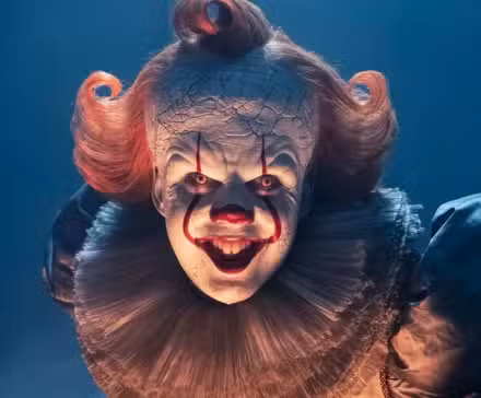Bill Skarsgard as Pennywise bending over and smiling for the camera in It: Welcome to Derry.