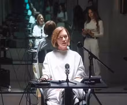 Sinatra seated for questioning with Gabriela reflected in the mirror behind her in Paradise Season 2 Episode 3