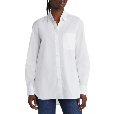 A woman wearing a white button-front blouse untucked, with blue jeans